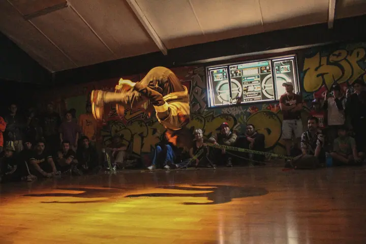 Un bboy gira en el aire sobre la pista, con el público sentado alrededor