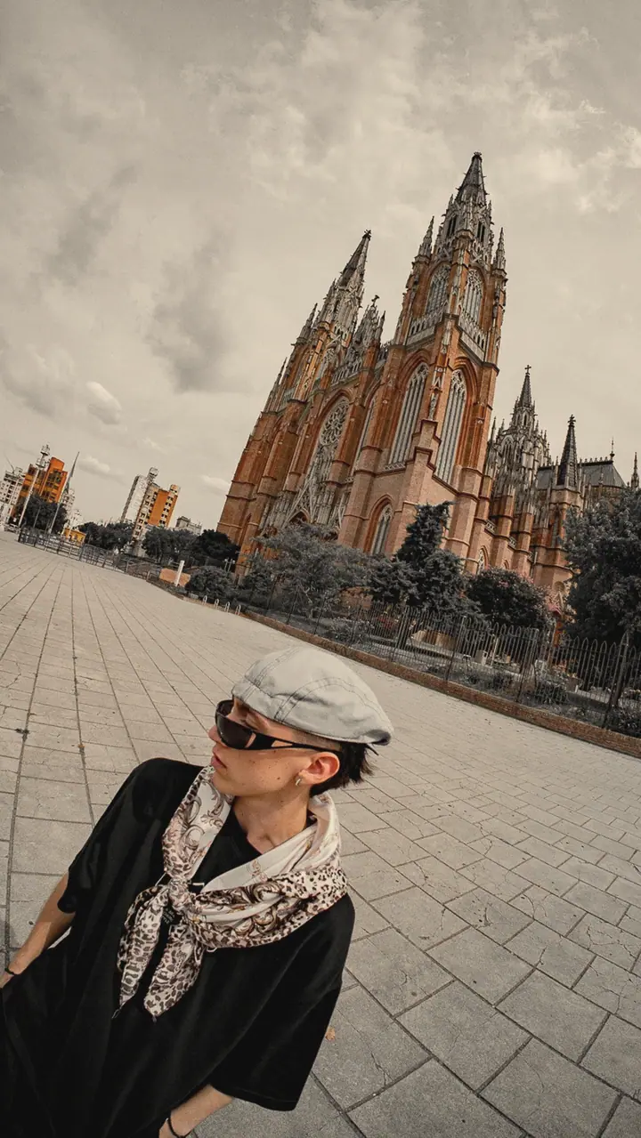 Nykotis agachado frente a la catedral, con lentes y gorra