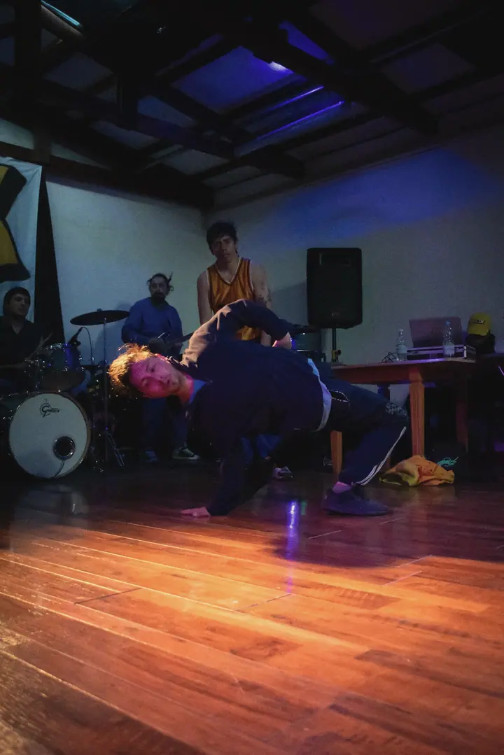 Un bailarín girando en el piso bajo luz azul, con la batería al fondo